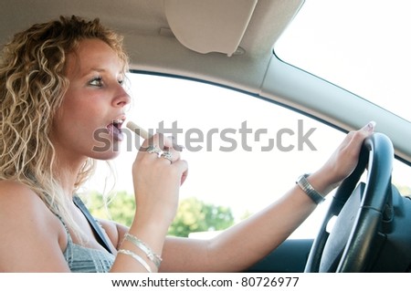 Young blond woman driving car and eating sweet - open mouth