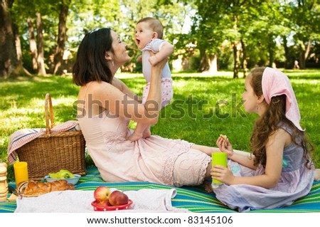 Mother and her two children having picnic in park, playing with baby