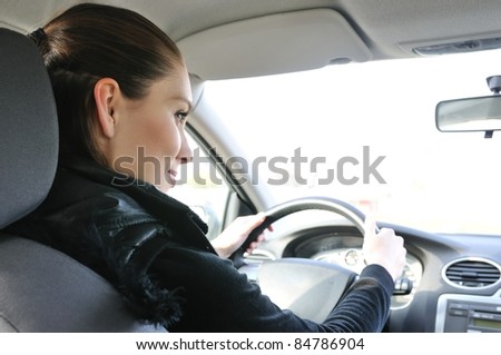 Lifestyle shot of young cheerful woman driving car - rear view