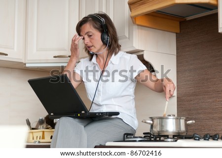 Young business woman having work conference call from home while cooking meal in kitchen