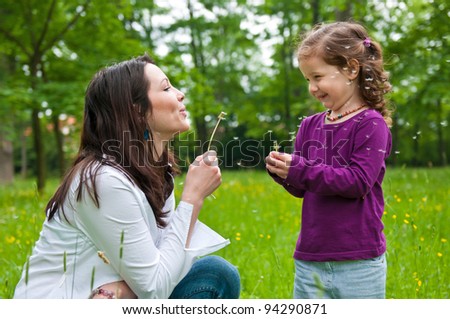Mother with small daughter blowing to dandelion - lifestyle outdoors scene in park
