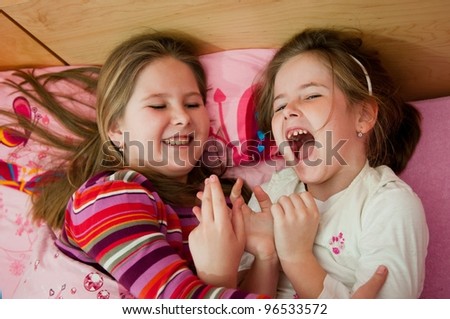 Cute children (two sisters) laughing at home lying in bed