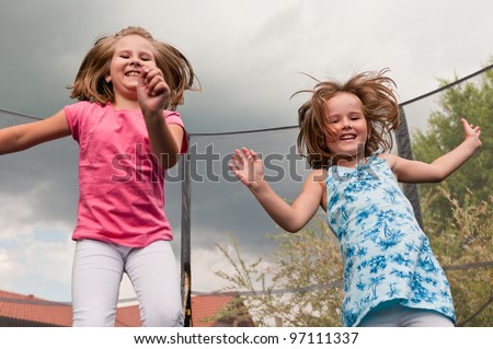 Small cute children jumping on trampoline - garden and family house in background