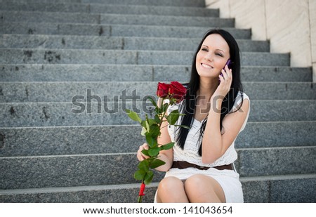 Young beautiful woman with red roses calling with mobile phone