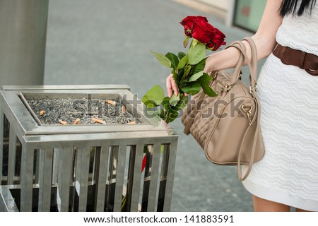 Young woman throws away red roses to litter bin, close-up