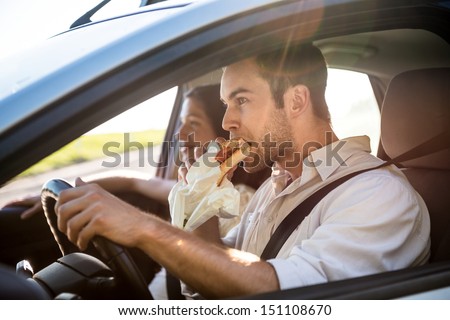 Couple in car - man is driving and eating baguette