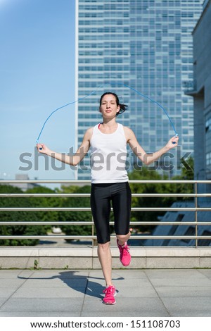 Young sport woman exercising with skipping rope in urban environment