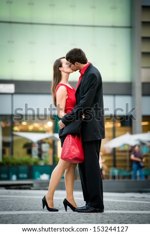 Young business couple dressed in red kiss and welcome each other on street