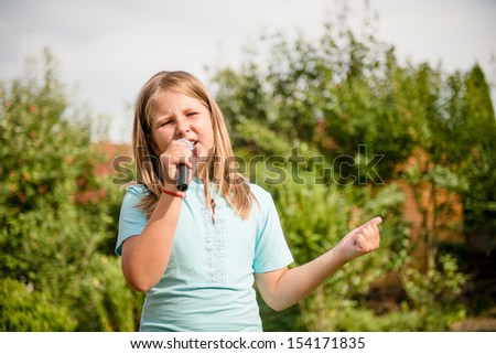 Happy childhood - child singing with microphone outdoor in backyard