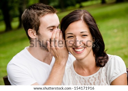 Young man whispering to woman (girlfriend) - outdoor lifestyle photo