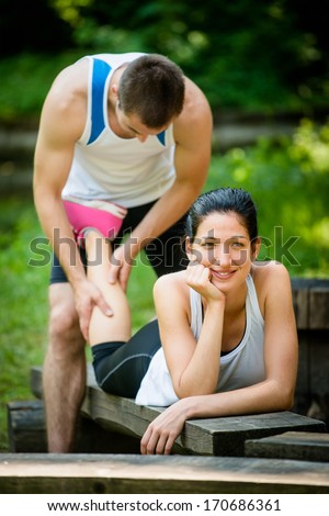 Man gives massage of calf to his girlfriend after sport training - woman lies on bench