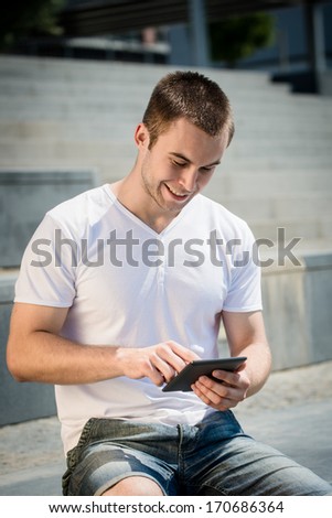 Young man reading book on electronic book-reader in urban environment