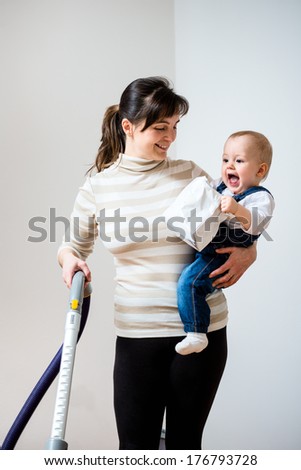 Cleaning up the room - mother with vacuum cleaner holding her baby on hands