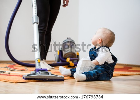 Cleaning up the room - woman with vacuum cleaner, baby sitting on floor