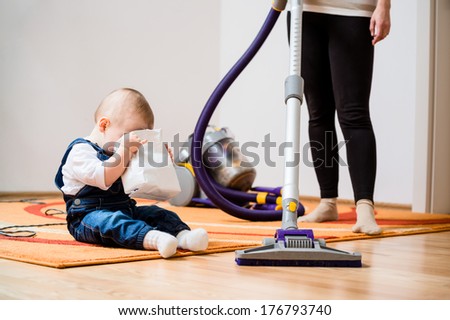 Cleaning up the room - woman with vacuum cleaner, baby looking to biscuits packet