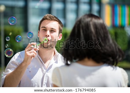 Man is blowing bubbles from bubble blower on his girlfriend - rear view