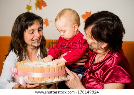 Mother and grandmother with baby celebrating first birthday - child damaging cake
