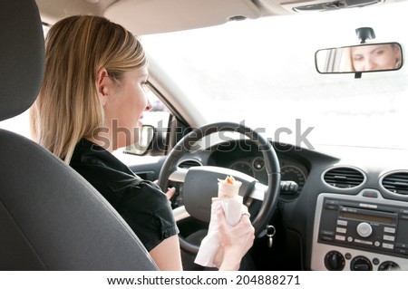 Young beautiful smiling woman driving car and eating fast food - rear view
