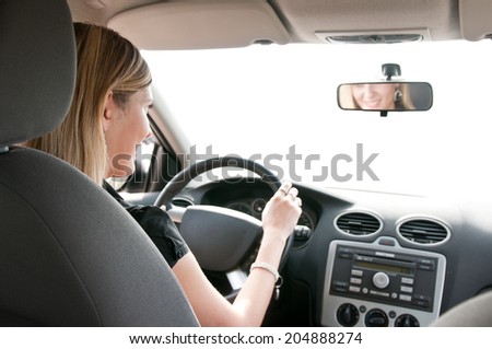Young cheerful woman driving car - rear view, reflexion of mouth in mirror