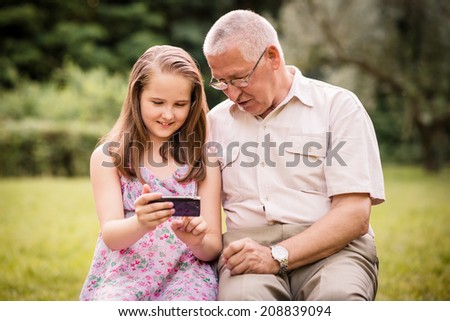 Senior man with his grandchild looking together on photos in smartphone - outdoor in nature
