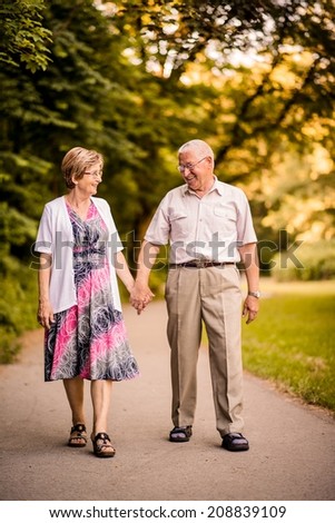 Happy senior couple walking together holding hands in forest park
