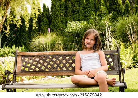 Outdoor child portrait - little girl sitting on bench outdoor in backyard