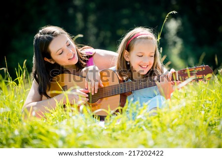Mother teaches playing guitar her child - outdoor in nature on sunny day