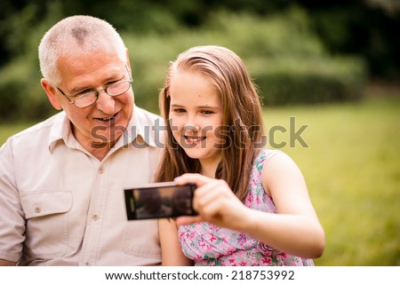 Girl taking photo with mobile phone of herself and her grandfather