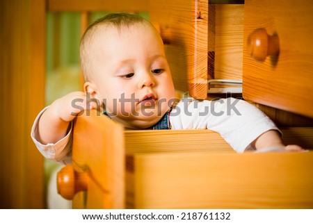 Baby opening drawer with clothes on wooden furniture - home interior