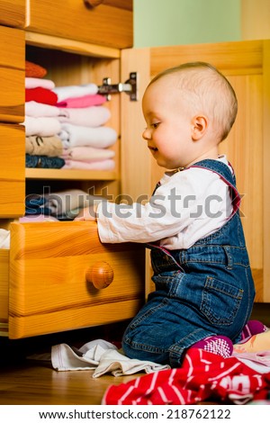 Baby throws out clothes from wooden furniture at home