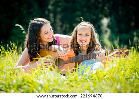Mother teaches plaing guitar her child - outdoor in nature on sunny day