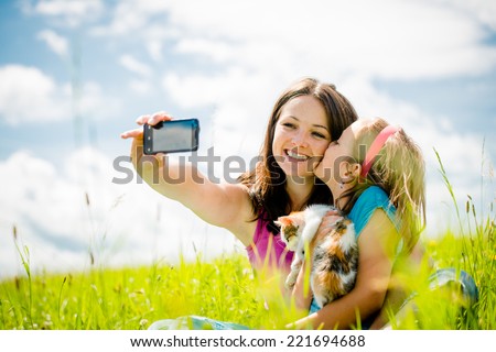 Young woman taking photo with her smart-phone camera of herself, her daughter and kitten