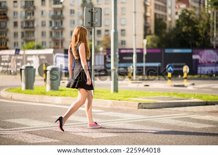 Young woman walking street - one foot in sneaker and other in high heel shoe