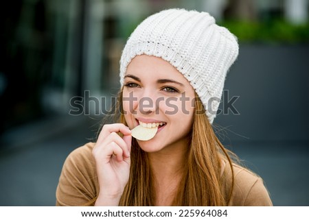 Teenager girl in cap eating chips outdoor in street