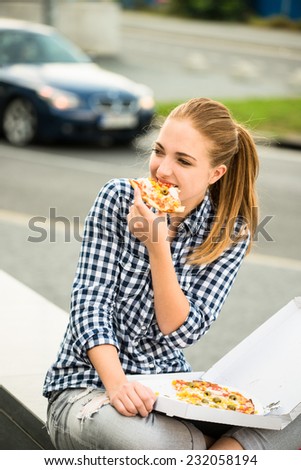 Teenager lifestyle - young woman eating pizza outdoor in street