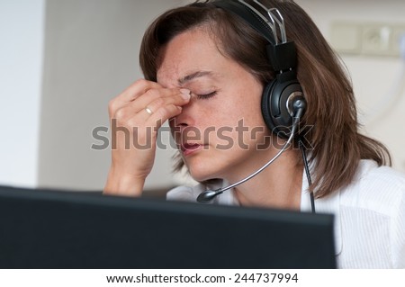 Young business person with headache working with computer(headset on head)