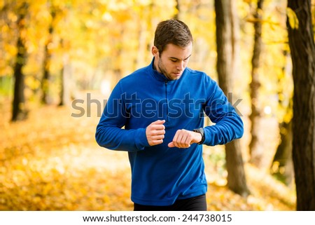 Young man jogging in beautiful fall nature and checking pulse on watches