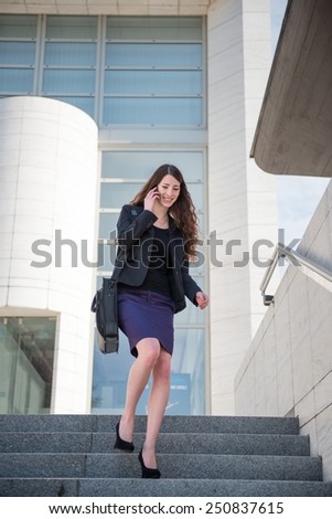 Young smiling business woman walking on stairs calling with mobile phone