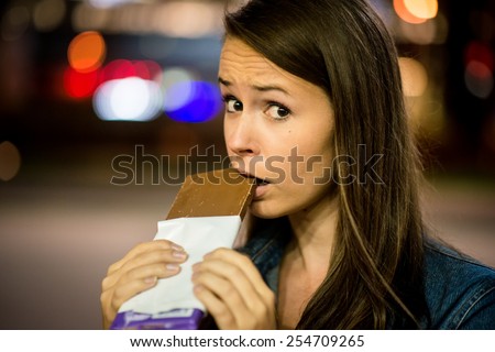 Young woman eating chocolate in street with neon lights at night