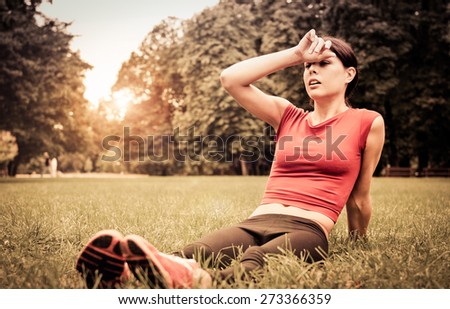 Relax in grass - tired woman sitting on grass after jogging at sunset