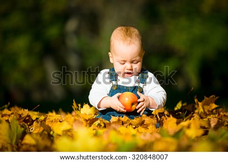 Cute baby eating apple outdoor in fall sunny day - sitting in leaves