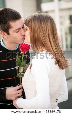 Young man handing over a flower (red rose) to woman and kissing her