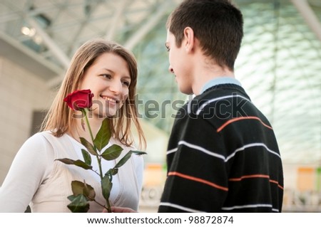 Young man handing over a flower (red rose) to woman - outdoor lifestyle scene