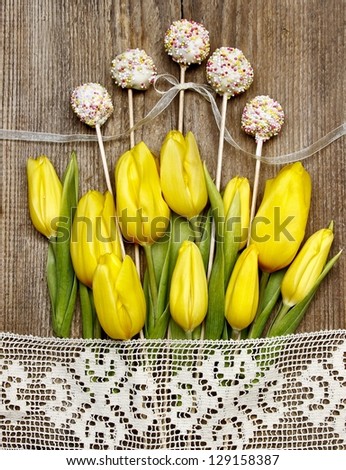 Cake pops on wooden background surrounded by yellow tulips