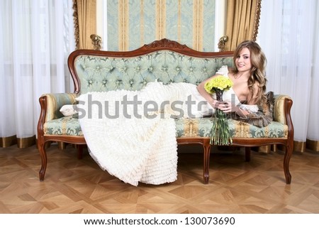 Beautiful, elegant bride lying on vintage sofa, holding bouquet of yellow flowers
