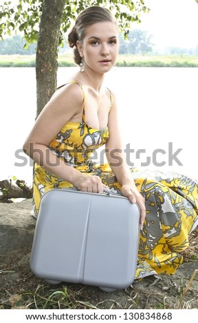 Tired young woman with traveling bag, resting under tree on hot summer day