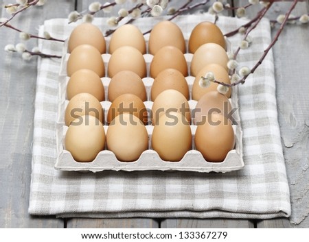 Group of fresh eggs in paper tray, on checked grey napkin, on old wooden, rustic table. Blooming willow in the background.