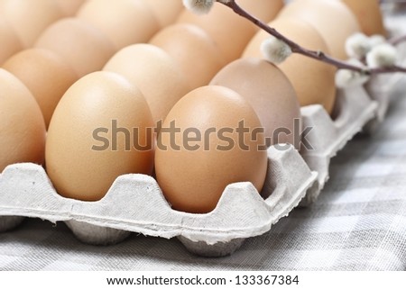 Group of fresh eggs in paper tray, on checked grey napkin, on old wooden, rustic table. Blooming willow in the background.