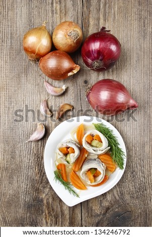 Top view of pickled herring rolls with vegetables on brown wooden background. Fresh onions and garlic, copy space.