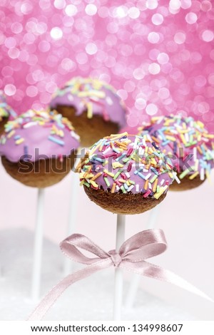 Pink cake pops decorated with colorful sprinkles. Pink glittering background, very festive.